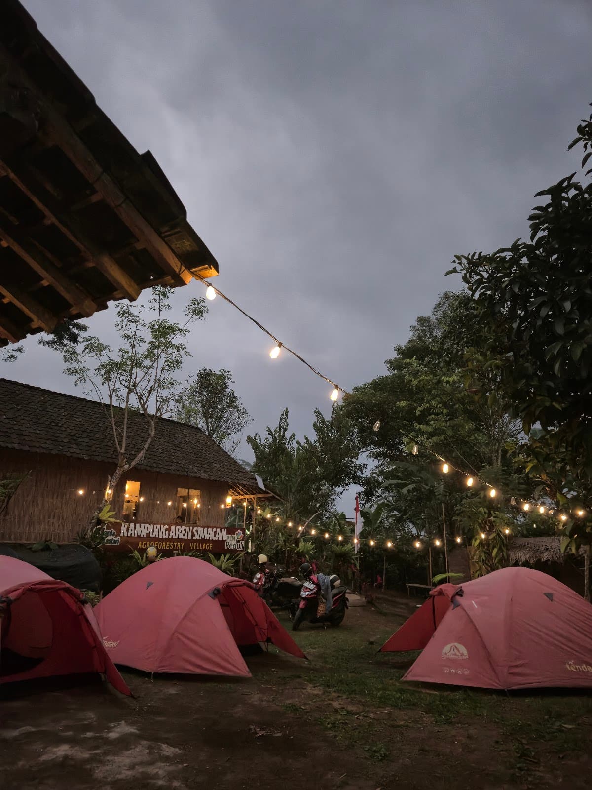 Camping ground Kampung Aren Simacan dengan tenda kubah berjajar di bawah rangkaian lampu, menjelang malam
