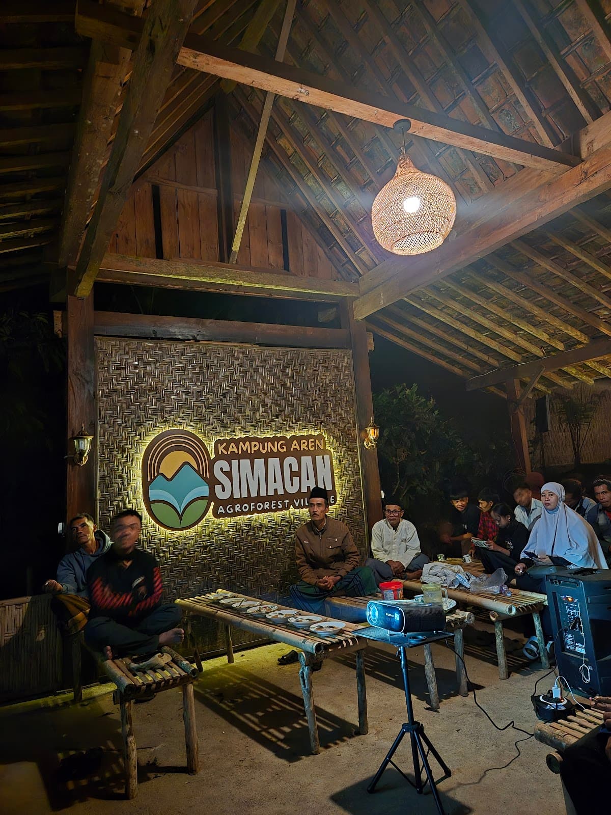 Warga Kampung Aren Simacan dalam pertemuan malam di balai bambu dengan proyektor menyala